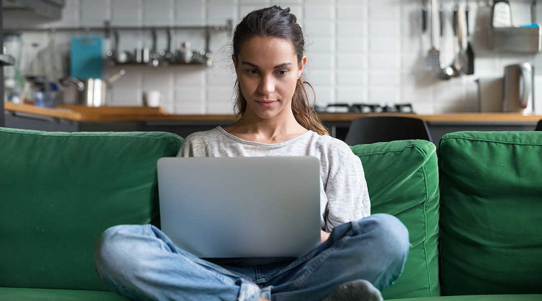 girl sitting cross legged on the couch looking down at her laptop